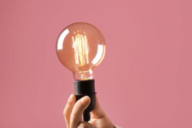 Pembe arka planda ampulü tutan erkek el, yakın plan.