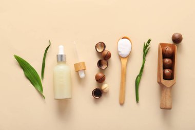 Macadamia fındıkları, yeşil yapraklar, ahşap kepçe ve bej arka planda bir şişe kozmetik ürünü.