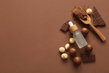 Macadamia fındığı, çikolata, kakao, ahşap kepçe ve kahverengi arka planda bir şişe kozmetik ürünü.