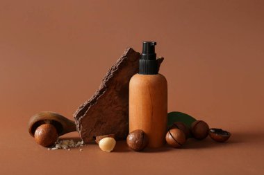 Kahverengi arka planda Macadamia fındığı, ağaç kabuğu ve bir şişe kozmetik ürünü.