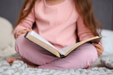 Yatakta oturup İncil okuyan tatlı küçük kız, yakın çekim.