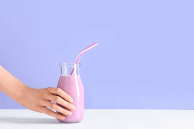 Mavi arka planda bir şişe taze smoothie ile kadın eli.