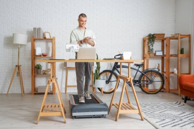 Ofisteki koşu bandında cep telefonuyla çalışan genç adam.