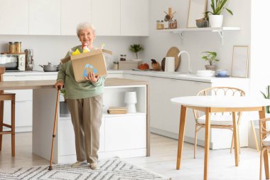 Mutfakta çöp kutusu olan yaşlı bir kadın. Atık sıralama kavramı