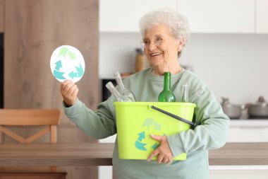 Mutfakta çöp tenekesi ve geri dönüşüm tabelasıyla kıdemli kadın. Atık sıralama kavramı