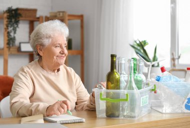 Evinde not defteri ve çöp bidonları olan yaşlı bir kadın. Atık sıralama kavramı