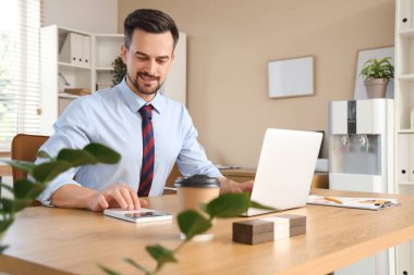 Ofisteki masada dizüstü bilgisayar ve hesap makinesiyle çalışan erkek muhasebeci.