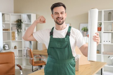 Ofiste kaslarını gösteren gerilmiş film rulosu olan erkek işçi.