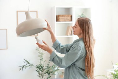 Evdeki tavan lambasına ampul takan genç bir kadın.