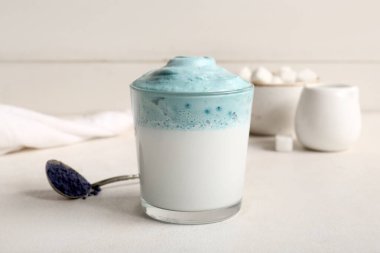 Bir bardak mavi dalgona matcha latte ve çay kaşığı beyaz masada toz kibrit, yakın plan.