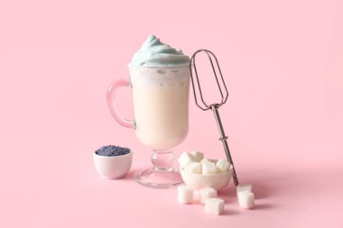 Bir bardak mavi dalgona matcha latte, bir kase pudra kibrit ve pembe arka planda rafine şeker.