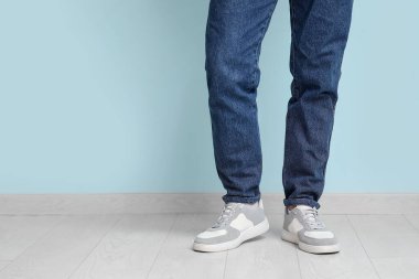 Mavi duvarın yanında şık ayakkabılı genç adam, yakın plan.