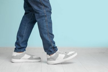 Mavi duvarın yanında şık ayakkabılı genç adam, yakın plan.