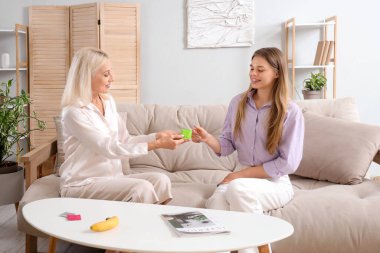 Prezervatifli bir anne, kızıyla evdeki koltukta seks eğitimi hakkında konuşuyor.