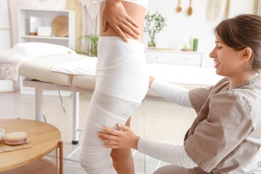 Masaj terapisti spa salonunda kadın vücudunu bandajlıyor.