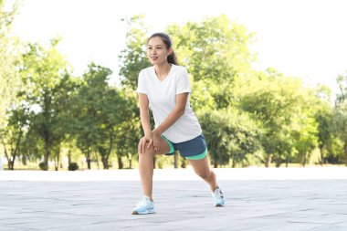 Güzel, genç, mutlu, sportif Asyalı kadın parkta koşarken esniyor.