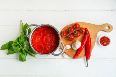 Beyaz ahşap arka planda fesleğen, sarımsak ve biberli domates sosu pişirmek.