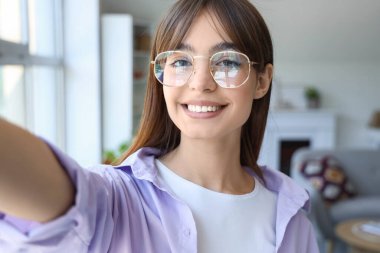 Gözlüklü genç kadın evde selfie çekiyor, yakın plan.