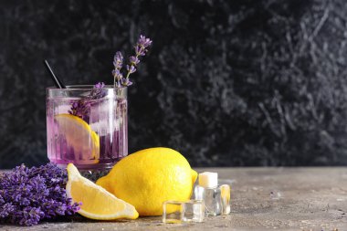 Bir bardak taze lavantalı limonata, çiçekler ve limonlar gri masada.