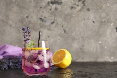 Bir bardak taze lavantalı limonata ve siyah masa üzerinde çiçekler.