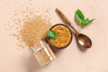 Tahta bir kase Dijon hardal, fesleğen ve bej arkaplanda tohumlar.