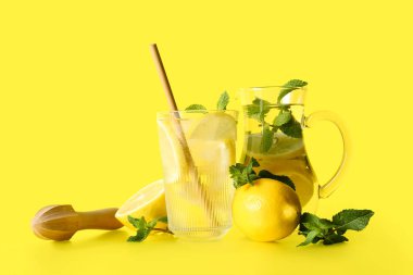 Sarı zemin üzerinde nane ve ahşap sıkacağı olan bir şişe taze limonata.