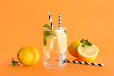 Bir bardak taze limonata, nane ve turuncu arka planda meyveler.