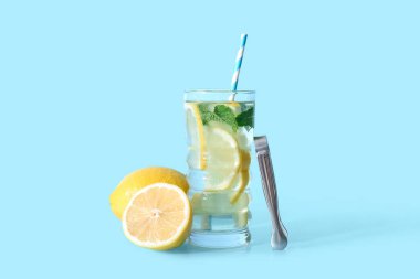 Bir bardak taze limonata, naneli ve mavi arka planda meyveler.