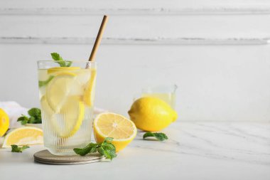 Bir bardak taze limonata, nane ve beyaz arka planda meyveler.