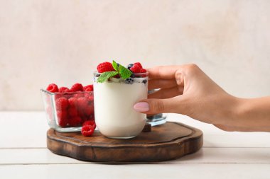 Elinde bir bardak lezzetli yoğurt ve beyaz arka planda farklı taze böğürtlenler tutan kadın.