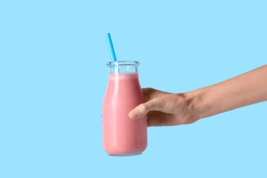 Mavi arka planda bir şişe taze pembe smoothie ile kadın eli.