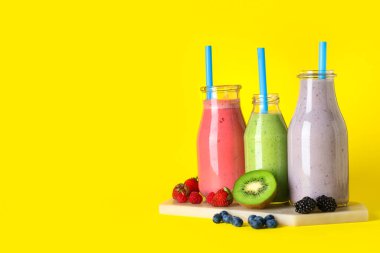Sarı arka planda farklı böğürtlenli taze meyve suyu şişeleri.