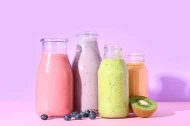 Farklı taze meyve suyu şişeleri kivi ve leylak arkaplanlı yabanmersini.