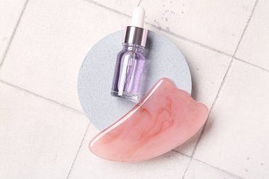 Alçı standı, kozmetik ürün şişesi ve fayans arka planında guasha masaj aracı, yakın çekim