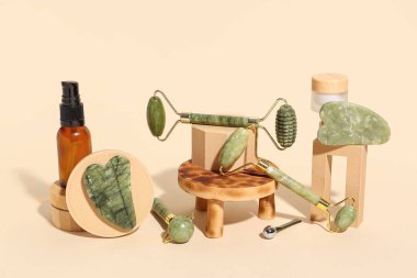 Farklı yüz masajı aletleri, alçı tezgahları, bej arka planda şişe ve kozmetik ürünler.