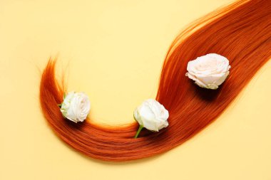 Kızıl saç teli ve soluk sarı arka planda çiçekler, yakın plan.