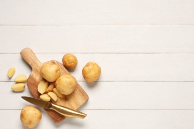 Beyaz ahşap zemin üzerinde çiğ patates ve bıçak olan tahta.