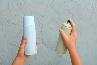 Renk duvarının yanında sprey boya kutularıyla kadın elleri, yakın plan.