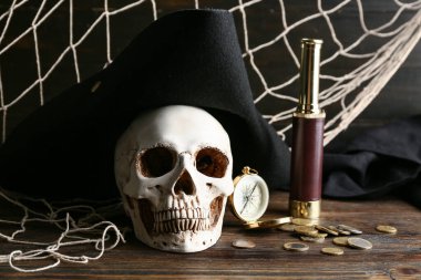 Korsan şapkalı kafatası, pusula, dürbün ve paralar ahşap masada.