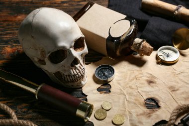 Koyu ahşap arka planda dürbünlü, romlu, pusulalı ve bozuk paralı kafatası, yakın plan. Korsan konsepti