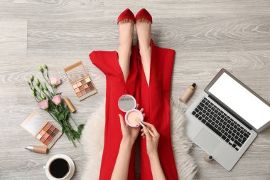 Kozmetik ürünleri ve dizüstü bilgisayarıyla ahşap zeminde makyaj sanatçısı.