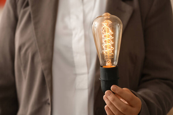 Young woman holding glowing retro light bulb, closeup