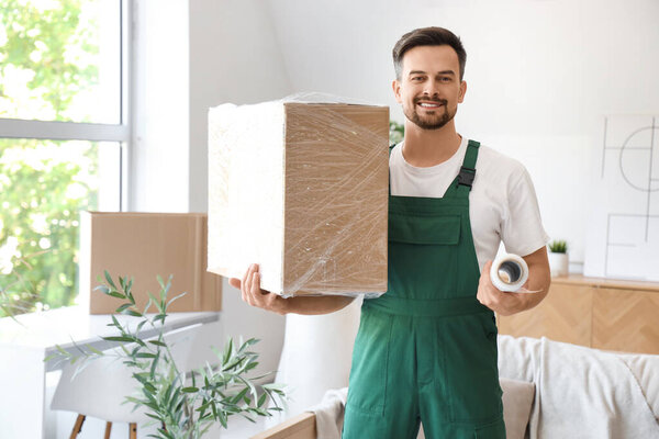 Работник мужского пола с рулоном стретч-пленки и коробкой в комнате