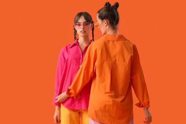 Turuncu arka planda şık kıyafetler içinde güzel, genç, moda kız kardeşler.