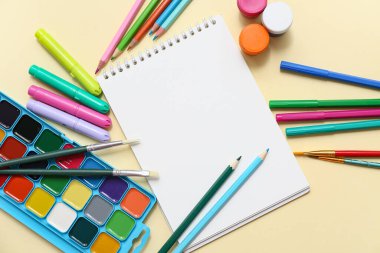 Renk arkaplanında boş defter, boya, kalem ve işaretleyicilerle kompozisyon