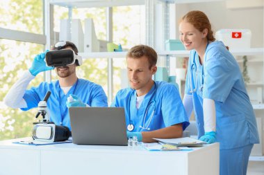 Klinikteki masada VR gözlüklü ve laptoplu genç doktorlar