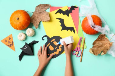 Malzeme ve yapıştırıcılı çocuk turkuaz arka planda Cadılar Bayramı süslemeleri yapıyor