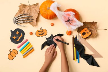 Sarı arka planda Cadılar Bayramı süslemeleri ve origami yarasaları yapan malzemeli çocuk