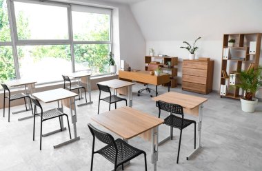 Sandalyeleri ve masası olan boş, şık bir sınıfın içinde.