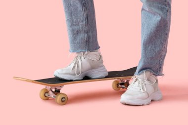 Beyaz spor ayakkabılı kadın bacakları ve pembe arka planda kaykaylı kot pantolon.